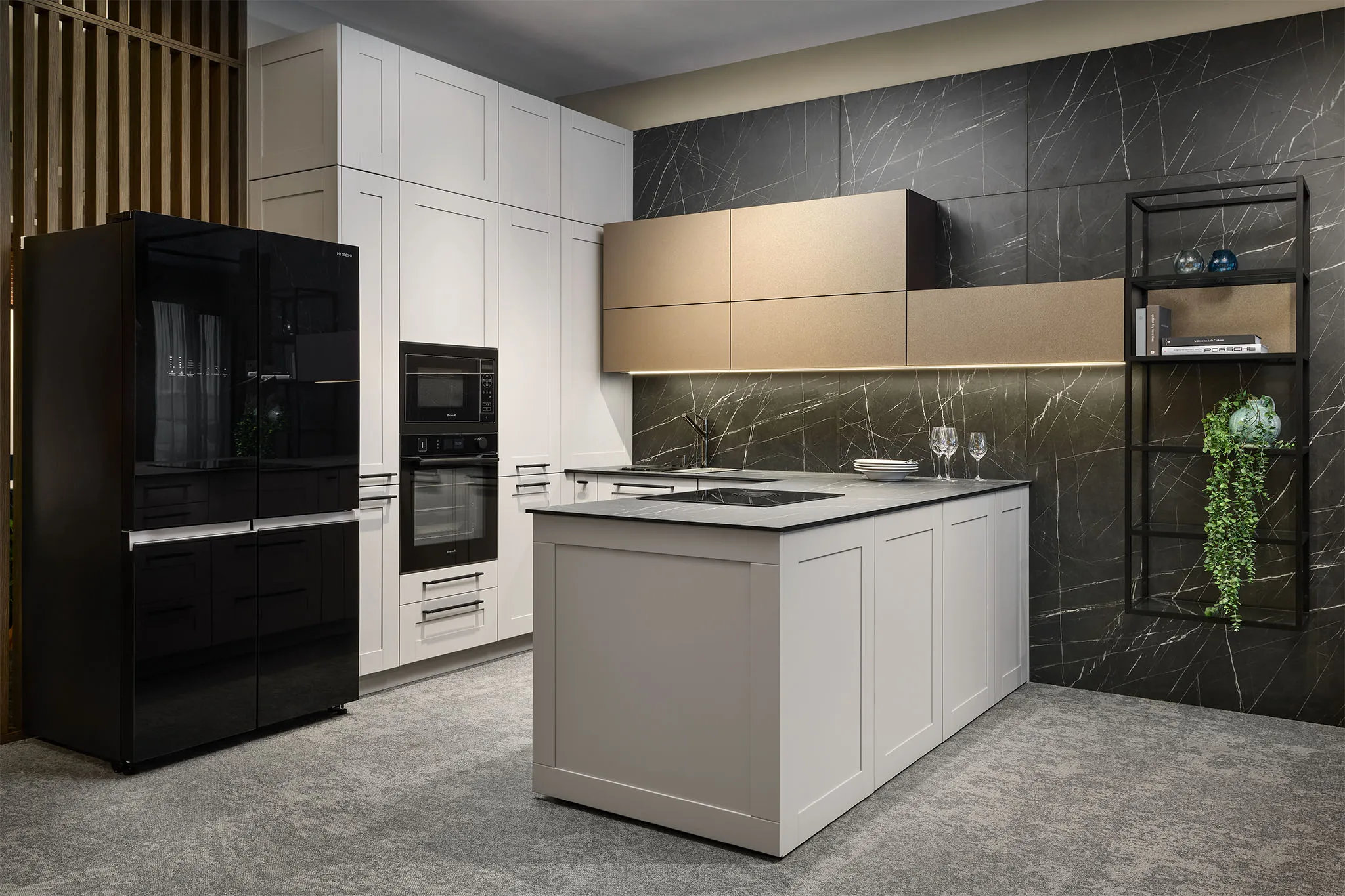 Moderní kuchyně s bílými rámovými skříňkami, černou lesklou lednicí a vestavnou troubou, centrálním ostrůvkem se světlou pracovní deskou, tmavým mramorovým obkladem stěny s podsvícenými horními skříňkami v béžovém odstínu a šedou podlahou v dekoru kamene.